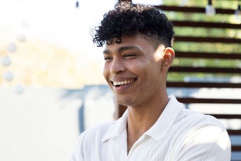 Smiling young african american man standing on sunlit patio wearing white collared shirt