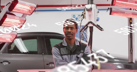 Confident automotive technician standing under infrared curing lamps in repair bay
