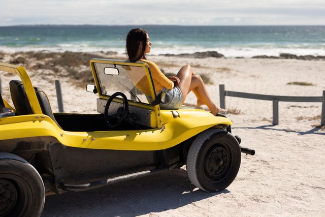 Caucasian woman sitting on beach buggy admiring the view on sunny beach by the sea. beach stop off on summer holiday road trip.