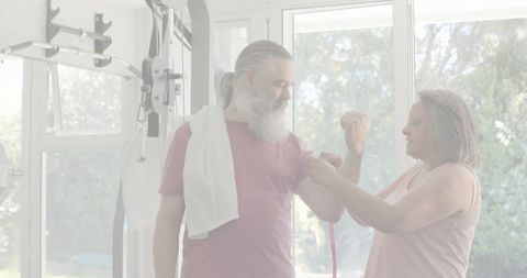 Couple measuring biceps in home gym, man flexing while partner uses tape measure