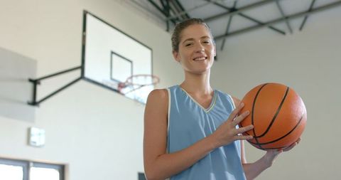 Female basketball player holding basketball in gym below hoop