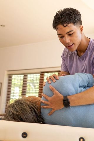 Therapist Adjusting Senior Asian Woman on Table in Bright Room