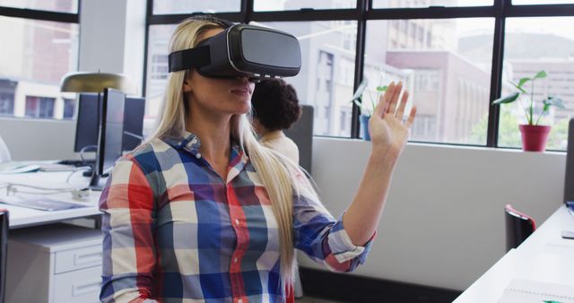 Young woman using virtual reality headset in modern office. Great for illustrating technological advancements, innovation in the workplace, and the integration of VR technology in various settings. Suitable for use in articles or advertisements about technology, VR experiences, and modern work environments.