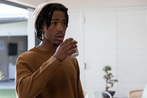 African american young man wearing beanie and brown quilted sweater holding coffee cup