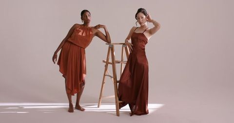 Elegant models in rust-colored satin dresses with studio ladder