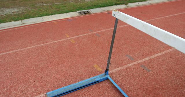 Image shows a close-up view of a metal hurdle on a red running track. Useful for illustrating themes related to athletics, hurdling training, running track facilities, sports competitions, and outdoor physical activities.