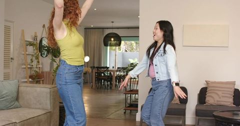 Diverse women laughing and stretching arms in modern open-plan living room with plants