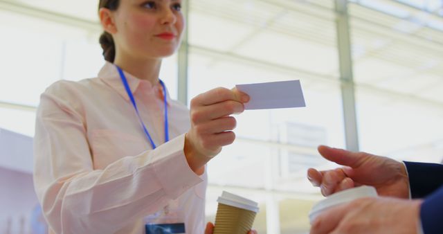 Businesswoman handing business card to another person during a coffee break, highlighting professional networking. Useful for illustrating corporate communications, business meetings, professional interactions, or office environments.