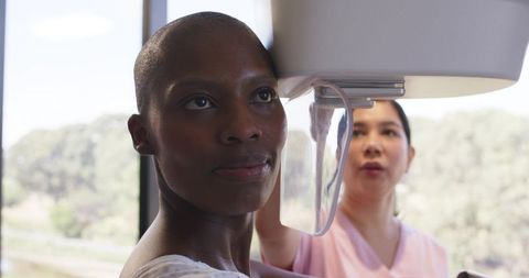 Female patient undergoing mammogram while technician adjusting paddle in modern clinic