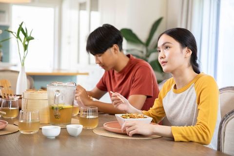 Asian Couple Enjoying Meal with Chopsticks and Tea at Home Kitchen Table