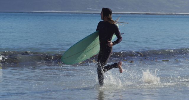 Woman running into the ocean with a surfboard, ready for a surfing adventure. Ideal for use in advertisements, travel blogs, adventure lifestyle promotions, and coastal tourism campaigns. Captures excitement, freedom, and outdoor activity.