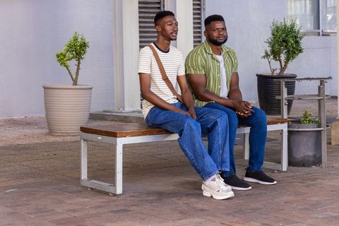 Two african men sitting on bench outdoors, casual conversation and urban friendship in daylight