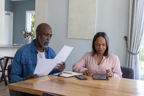 African american couple reviewing finances at dining table using tablet and documents