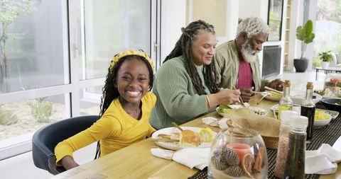 Multigenerational Black family enjoying sunlit lunch around wooden table with smiling child