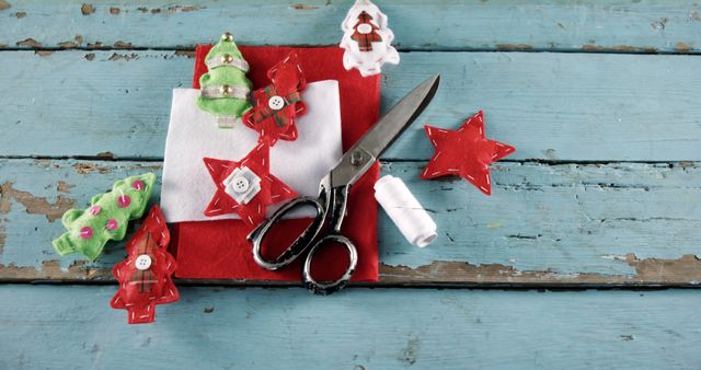 A variety of Christmas-themed decorations and scissors are laid out on a red cloth over a rustic blue wooden surface, with copy space. Festive crafting materials suggest preparations for holiday activities or DIY projects.