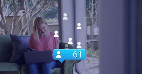 A woman sitting on sofa multitasking by using her laptop and engaging with digital media icons. Enhanced by digital overlay, the concept of connectivity and social media interaction is emphasized. Ideal for uses in technology marketing, social networking campaigns, and articles about connected lifestyles and work-from-home scenarios.