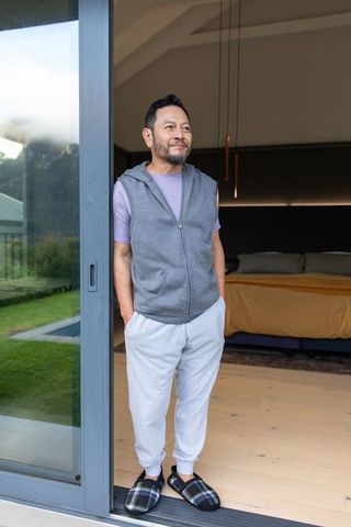 Contemplative mature asian man standing at sliding door looking outward, cozy modern home