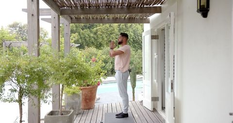Man practicing yoga on deck under pergola by pool outdoors
