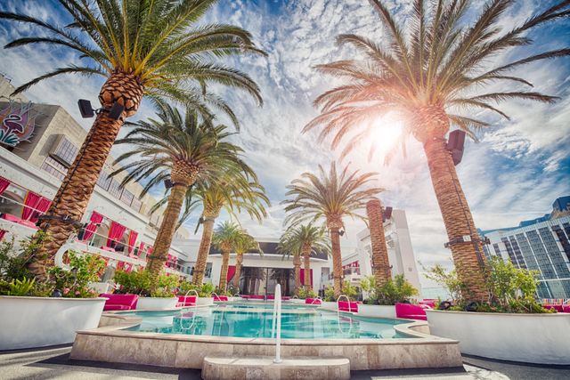 Luxurious poolside with palm trees on terrace and elegant lounge area under blue sky. Ideal for travel and tourism promotions, vacation advertisements, luxury lifestyle content, and resort marketing materials.