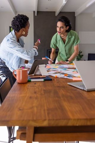 Diverse creatives collaborating on design layouts at wood table with markers and tablet