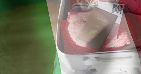 Packing passport and boarding pass in white carry-on with pink knit sweater, travel essentials