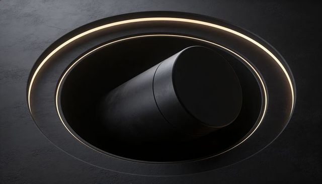 Tilting matte black cylinder with glowing concentric rings in minimalist dark interior