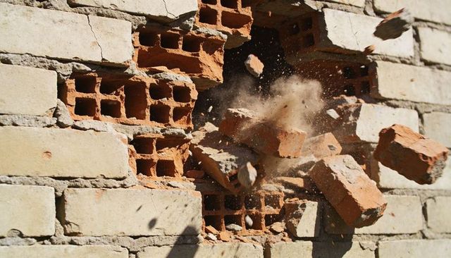 Breaking brick wall sending flying debris and dust from masonry breach