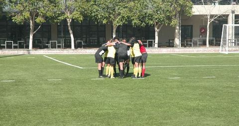 Youth soccer team huddles in celebration on sunny field
