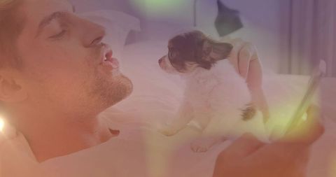 Man relaimg in bedroom balancing small puppy and holding smartphone
