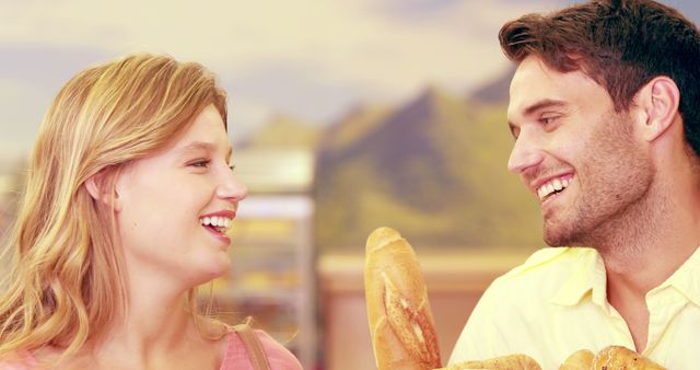 A young Caucasian couple shares a joyful moment in a bakery, surrounded by fresh bread, with copy space. Their smiles and eye contact suggest a warm, romantic connection as they enjoy each other's company.