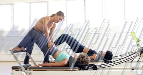 Pilates coach guiding two clients performing reformer bridge exercises in bright studio