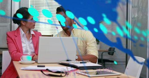Colleagues collaborating over laptop reviewing documents in modern office with data overlay