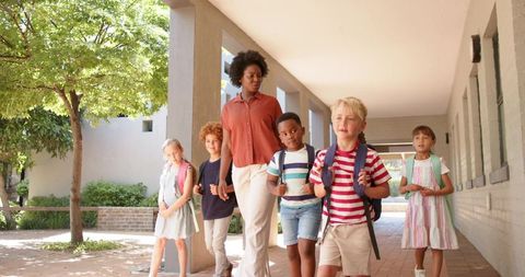 African american teacher guiding diverse elementary students along sunlit school colonnade