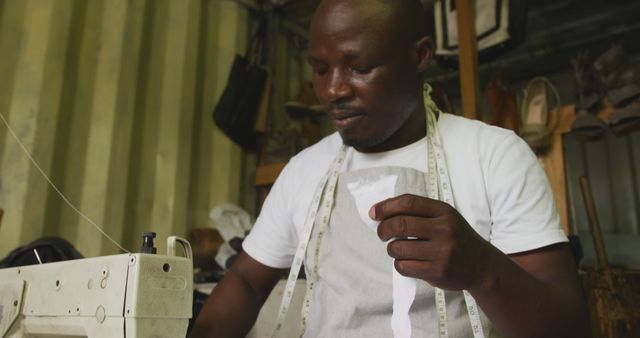 A skilled tailor measuring and preparing fabric while working on a sewing machine in a workshop. The image can be used for topics related to textile industry, craftsmanship, handmade clothing, small business, and artisan work.