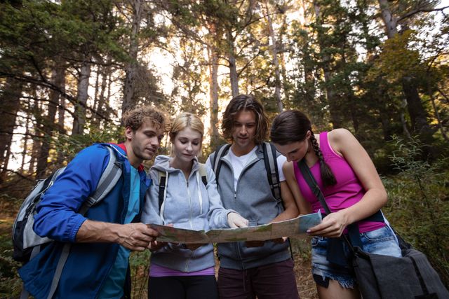 Group of friends studying a map while hiking in a dense forest. Ideal for themes related to outdoor adventures, teamwork, navigation, and nature exploration. Perfect for travel blogs, adventure tourism promotions, and outdoor activity guides.