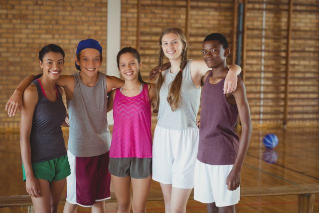 Diverse group of high school students standing together in a basketball court, smiling and showing camaraderie. Ideal for use in educational materials, sports promotions, youth programs, and advertisements focusing on teamwork and diversity.