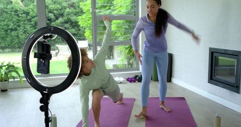 African american women practicing yoga with instructor and ring light for virtual fitness