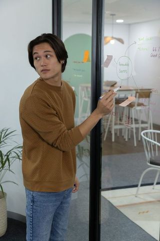 Asian man drawing renewable sources diagram on glass during team brainstorming