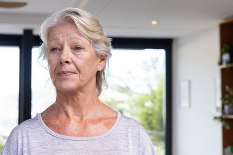 Pensive senior woman standing in bright modern home with minimalist decor and plants