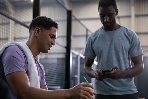 Friends resting after workout on indoor court, towel over shoulder and checking phone