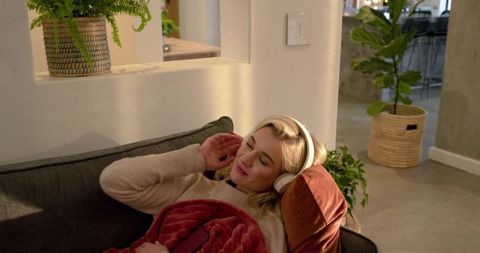 Relaxing woman listening to music with wireless headphones on cozy modern living room sofa