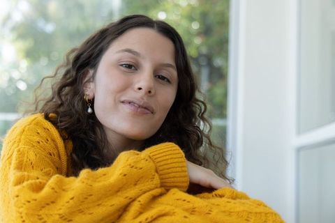 Serene woman leaning on folded arms wearing mustard cable-knit sweater by window