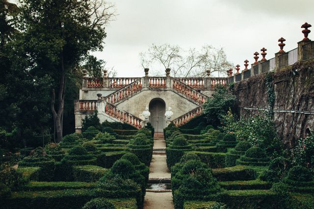 Elegant garden surrounded by lush greenery features well-crafted hedge maze with stone pathways leading to an ornate historic staircase. The scene captures a sense of timeless European charm. Useful for themes related to architecture, botany, history, travel, and outdoor landscapes in advertising, publications, and digital content.
