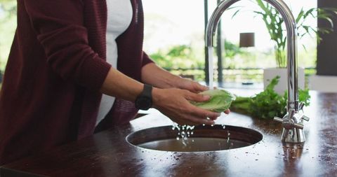 Pregnant Woman Washing Fresh Vegetables in Kitchen