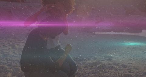Kneeling woman examining seashell on moody dusk beach with magenta light leak