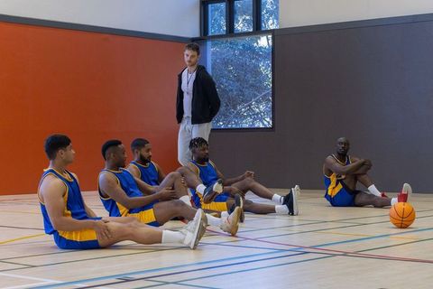 Basketball team members stretching on indoor court with coach