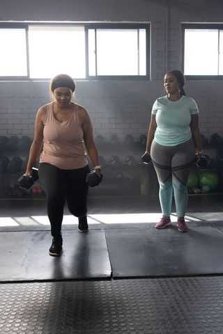 African american women working out with dumbbells in gym, strength training partners