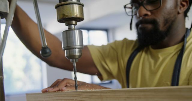 African American man operates a drill press in a workshop. He's focused on his woodworking project, demonstrating skill and precision.