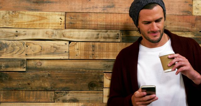 Man Wearing Beanie Holding Coffee and Checking Phone - Download Free Stock Images Pikwizard.com
