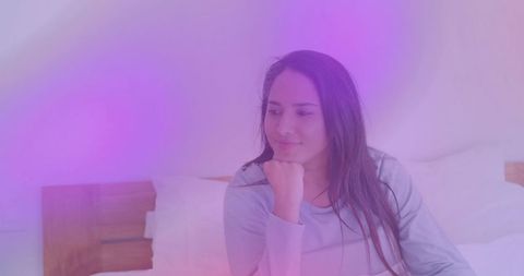 Resting Indian woman gazing thoughtfully in cozy bedroom with pastel mood lighting